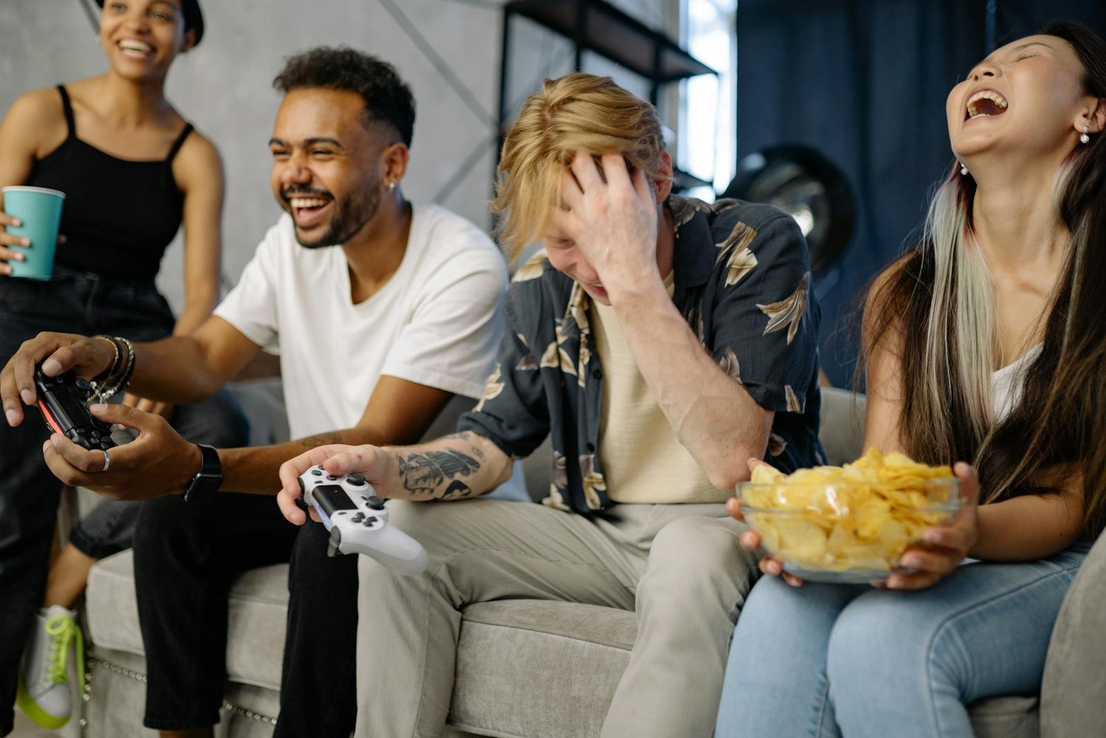 Diverse group of friends having fun playing video games indoors, sharing laughter and snacks.